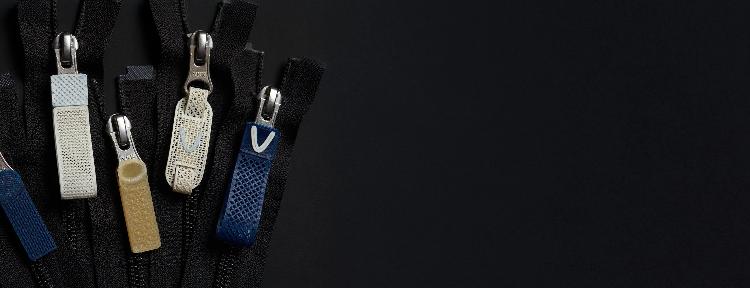 Composite zipper pullers in cream, tan and blue on black zip tape